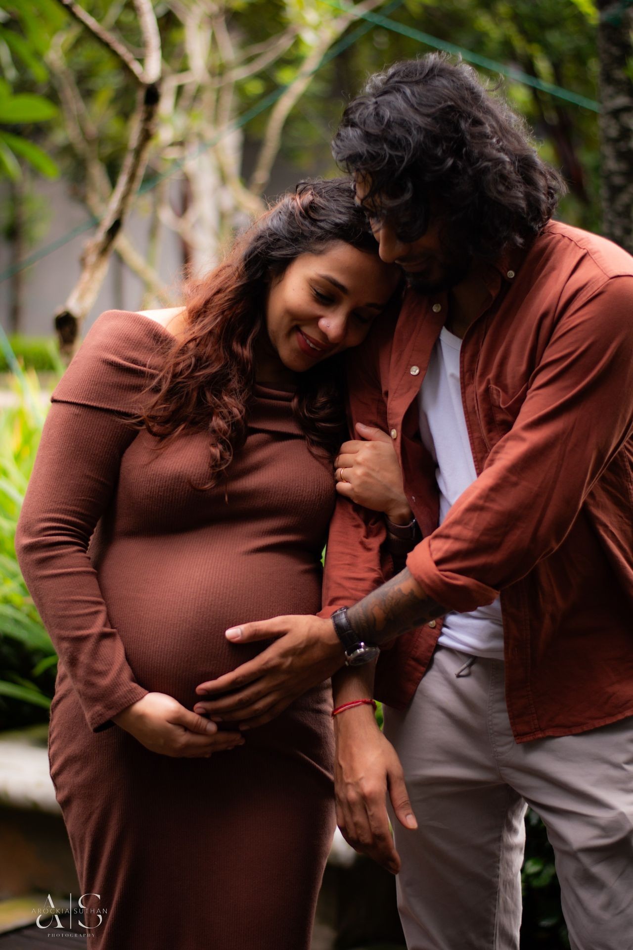 Man and pregnant woman embracing tenderly outdoors, the man's hand lovingly placed on the woman's belly.