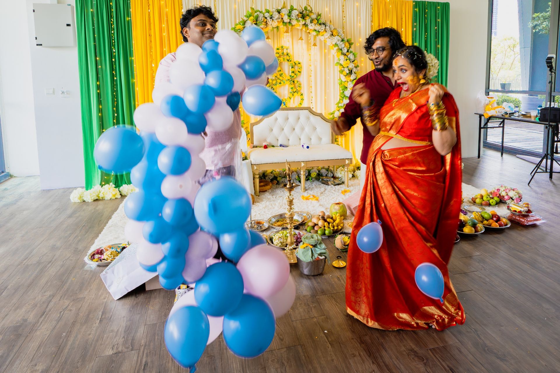 A festive setting with vibrant decorations, balloons, and traditional offerings on the floor.