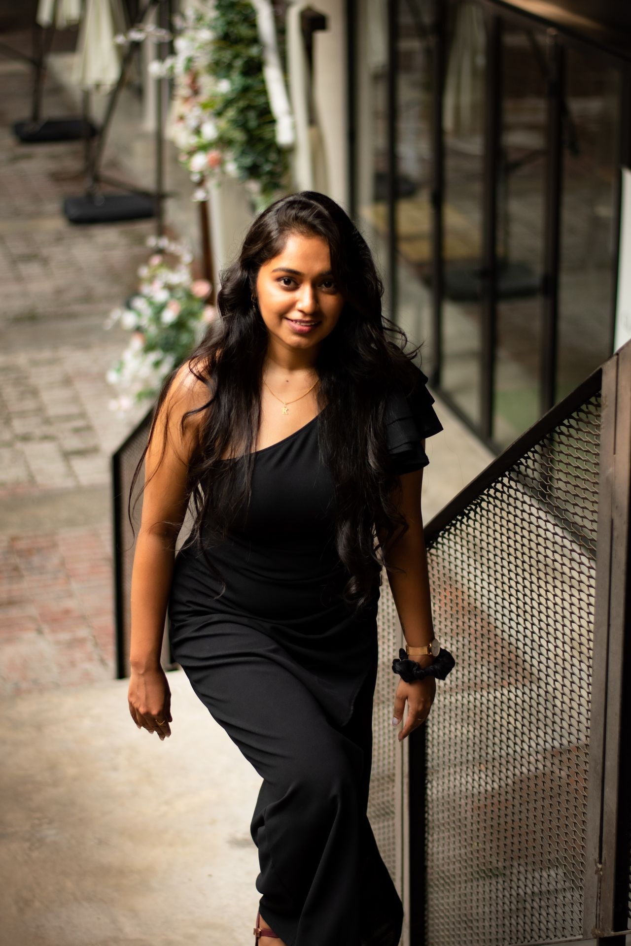 Woman in a black dress standing on stairs, with flowers and greenery in the background.