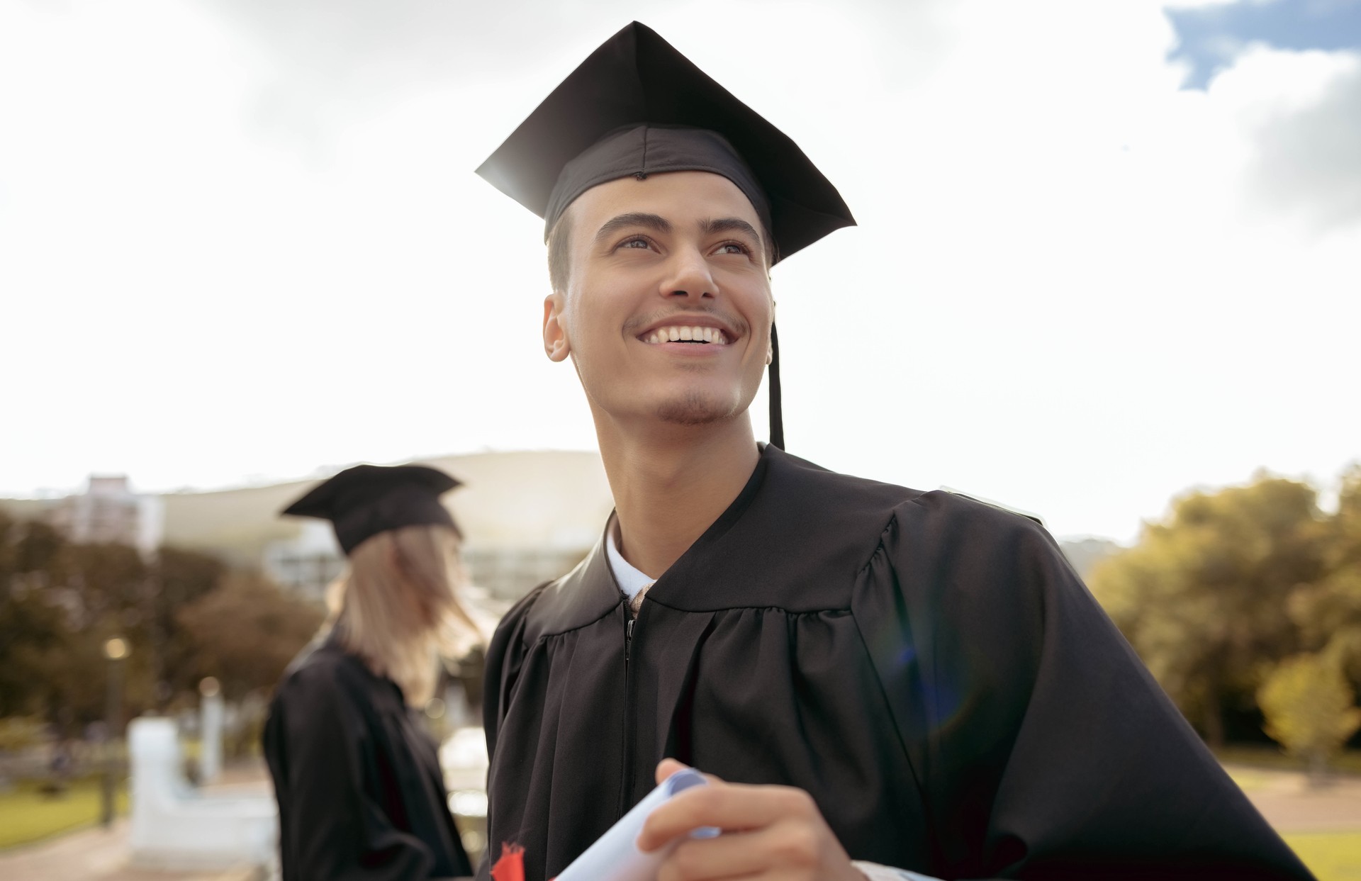 Graduation, happy man and thinking of success, achievement and study goals at outdoor college event. Graduate, education award and smile for future, dream and motivation of learning, hope and pride